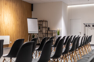 Interior of empty conference hall with black chairs, flipcharts and white screen. Selective focus. 
