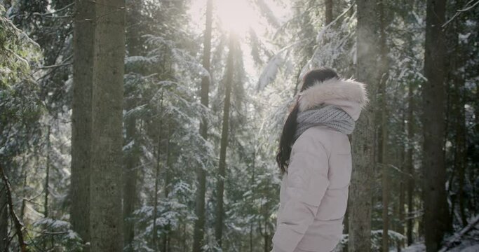 Unrecognizable bunette woman standing amid snow covered trees on frosty winter morning.