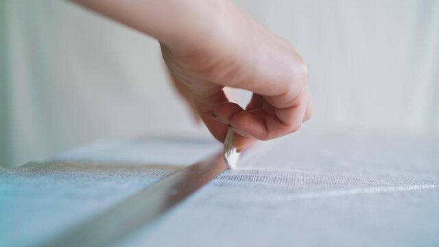 close up: woman makes cut dense fabric with chalk piece and metal ruler