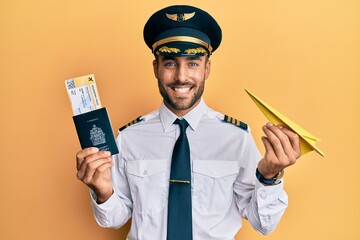Handsome hispanic pilot man holding paper plane and passport smiling with a happy and cool smile on face. showing teeth. © Krakenimages.com