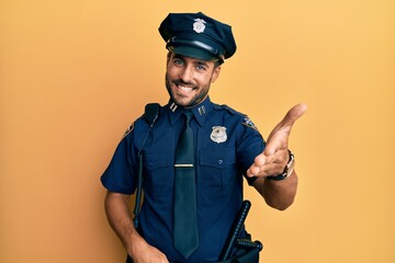 Handsome hispanic man wearing police uniform smiling cheerful offering palm hand giving assistance...