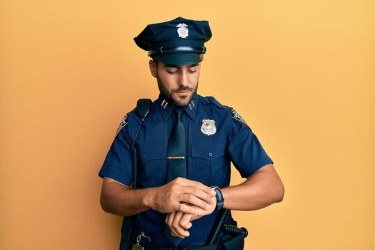 Handsome hispanic man wearing police uniform checking the time on wrist watch, relaxed and confident