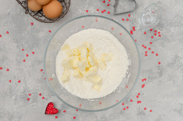 Preparing of heart-shaped cookies with pink chocolate glaze for Valentine's Day. Flour, powdered sugar, almond flour and butter in a bowl. Recipe step by step. Top view.
