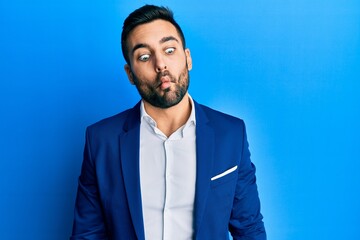 Young hispanic businessman wearing business jacket making fish face with lips, crazy and comical gesture. funny expression.