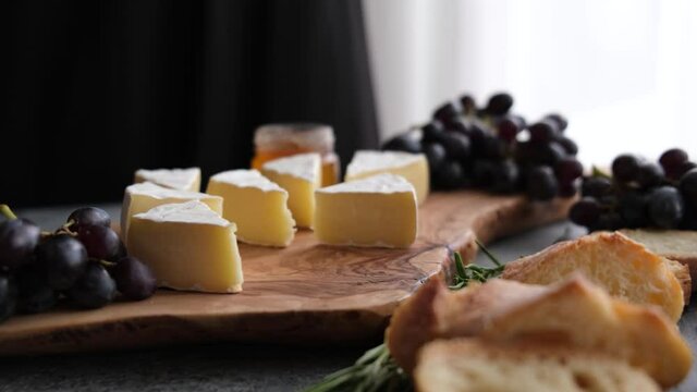 Brie or camembert cheese sliced on wooden cheeseboard served with grapes, figs and french bread
