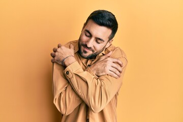 Young hispanic man wearing casual clothes hugging oneself happy and positive, smiling confident. self love and self care