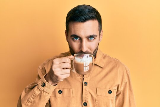 Handsome hispanic man enjoying a cup of coffee over yellow background