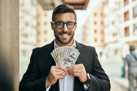 Young hispanic businessman smiling happy holding american dollars at the city.