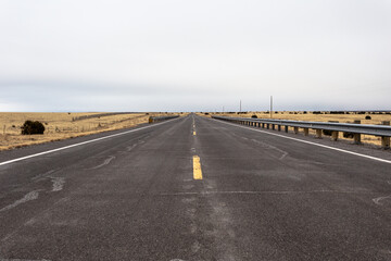 Low angle view of two lane road cutting through yellow fields in rural New Mexico on cloudy day