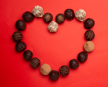 love concept image of heart shape made of chocolate truffles on red paper texture background