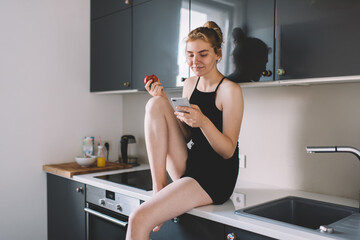 Cheerful female eating apple and browsing phone