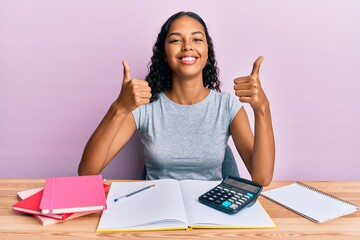 Young african american girl accountant working at the office success sign doing positive gesture with hand, thumbs up smiling and happy. cheerful expression and winner gesture.