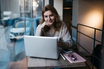 Cheerful young woman watching movie on laptop in modern cafe