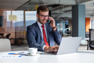 Portrait of a handsome businessman in eyeglasses talking on the phone with a client while sitting...