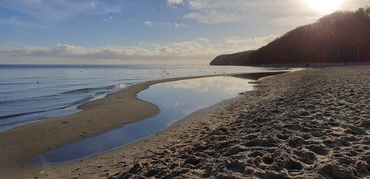 Sunny winter day in Gdynia, sandy beach with clouds reflecting in the calm see, boulevard and clifs on the horizon, Poland