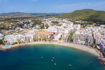 Fototapeta premium Aerial drone photo of the beautiful island of Ibiza in Spain showing the costal front golden sandy beaches with people relaxing and sunbathing on a hot sunny summers day