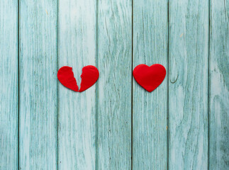 Two red hearts on wooden turquoise background. One heart is full and another heart is broken. Two different types of love stories concept.
