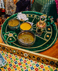 Mehndi round emerald green plate on table with open boxes of golden haldi for wedding henna party 