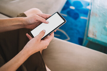 Crop faceless woman using smartphone while sitting on couch