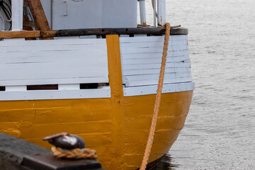 Stern of an old wooden boat with mooring rope tied to bridge. Thick white and yellow paint.