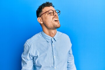 Young hispanic man wearing casual clothes and glasses angry and mad screaming frustrated and furious, shouting with anger. rage and aggressive concept.