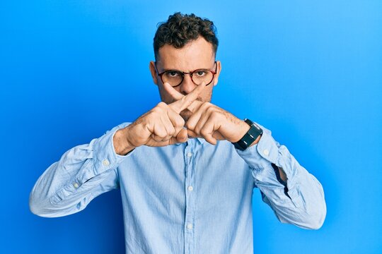 Young hispanic man wearing casual clothes and glasses rejection expression crossing fingers doing negative sign