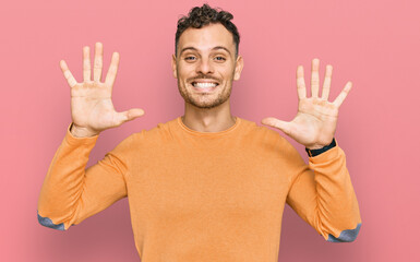 Young hispanic man wearing casual clothes showing and pointing up with fingers number ten while smiling confident and happy.