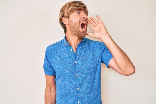 Young blond man wearing casual clothes shouting and screaming loud to side with hand on mouth. communication concept.