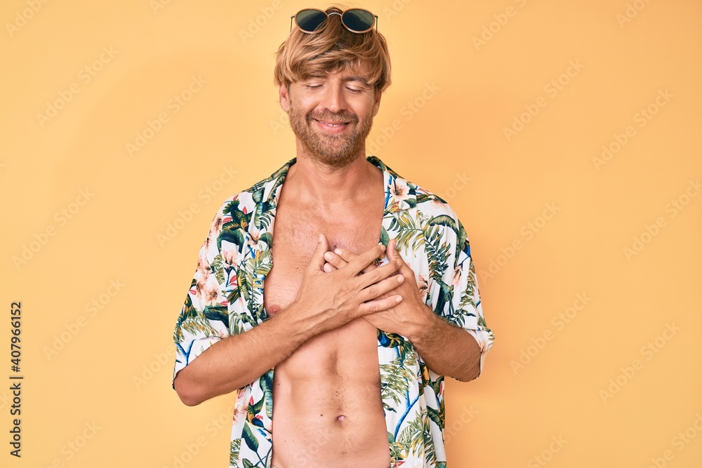 Poster young blond man wearing summer style smiling with hands on chest with closed eyes and grateful gestu