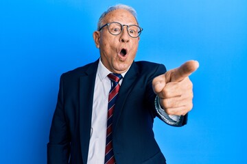 Senior caucasian man wearing business suit and tie pointing with finger surprised ahead, open mouth amazed expression, something on the front