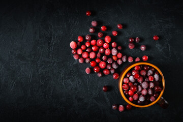 cranberries in a clay cup and sprinkled on a black plaster background. top view. artistic moody food concept with copy space