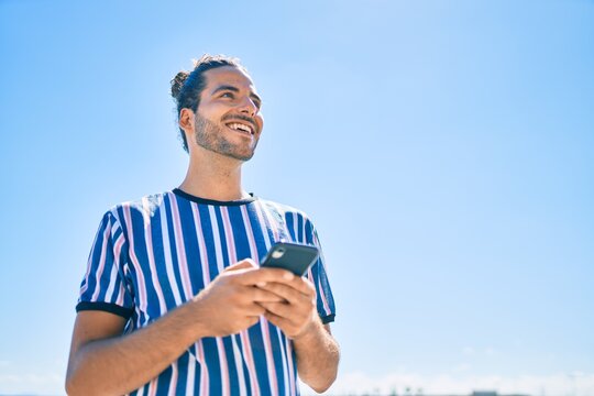 Young hispanic man smiling happy using smartphone at the beach.