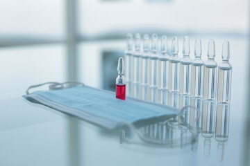 Vial with red and transparent vaccines medical protective mask on glass table in clinic