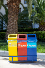 Three metal containers for different garbage with an inscription in english - paper, glass, plastic stand under the palm trees. Separation and sorting of rubbish