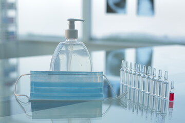 Vial with red and transparent vaccines medical protective mask and antiseptic on glass table in clinic