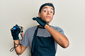 Young handsome african american man tattoo artist wearing professional uniform and gloves holding tattooer machine cutting throat with hand as knife, threaten aggression with furious violence