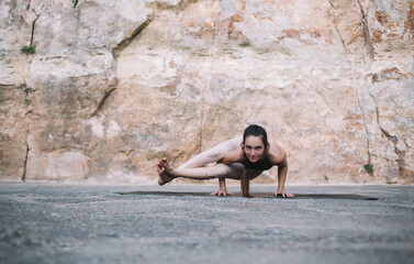 Focused young ethnic female performing Side Crow yoga pose in nature