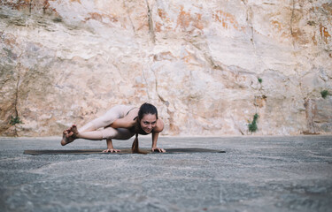 Strong young ethnic female standing on hands in Parsva Bakasana yoga position