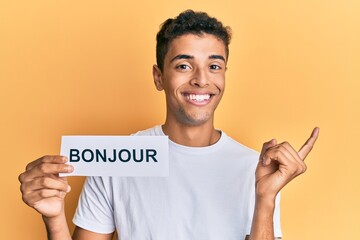 Young handsome african american man holding bonjour french greeting word smiling happy pointing with hand and finger to the side © Krakenimages.com