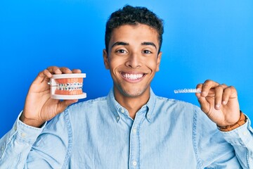 Young handsome african american man holding invisible aligner orthodontic and braces smiling with a happy and cool smile on face. showing teeth.