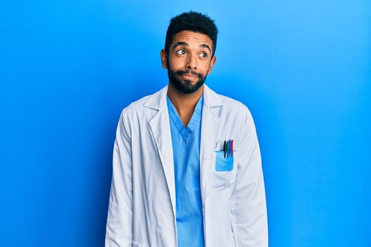 Handsome hispanic man with beard wearing doctor uniform smiling looking to the side and staring away thinking.