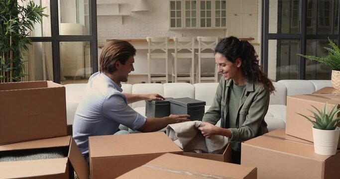 Happy smiling millennial family couple giving high five, finishing unpacking first carton box with personal stuff, celebrating moving into new home apartment, relocation real estate purchase concept.