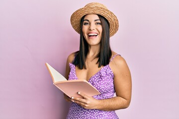 Young brunette woman reading book celebrating crazy and amazed for success with open eyes screaming excited.