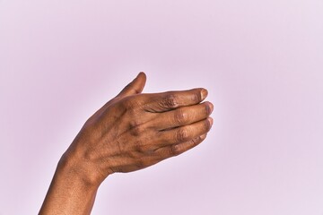 Arm and hand of black middle age woman over pink isolated background holding invisible object, empty hand doing clipping and grabbing gesture