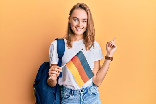 Beautiful blonde woman exchange student holding germany flag smiling happy pointing with hand and finger to the side