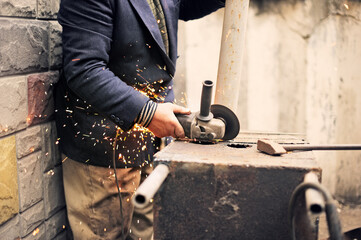 Closeup of the hands of a man processing an iron workpiece on the street with an angle grinder.