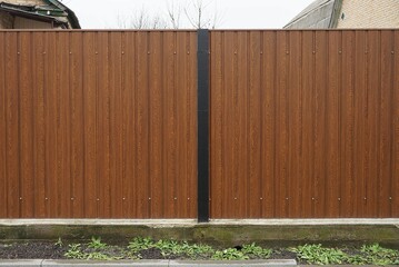 part of a brown metal fence wall with a black post on a rural street