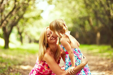 Obraz premium Little blonde girl kissing her blonde mother in the park