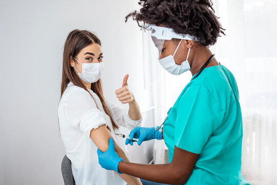 Girl Gesturing Thumbs-Up Receiving Coronavirus Vaccine Injection In Hospital. Covid-19 Vaccination.  Corona Virus Protection, Cure And Medication. Woman getting a COVID-19 vaccine