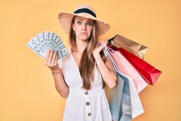 Young blonde girl holding shopping bags and dollars banknotes depressed and worry for distress, crying angry and afraid. sad expression.